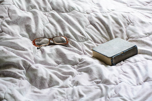 beyaz bir battaniye üzerinde gözlük ve bir kitap vardır. Aydınlatma - gün ışığı. Konsept - yatakta sabah - Fotoğraf, Görsel