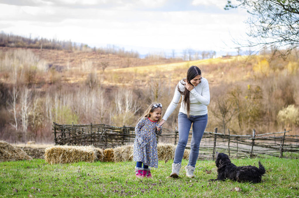 Genç anne ve kızı kırsalda köpekle eğleniyor. - Fotoğraf, Görsel