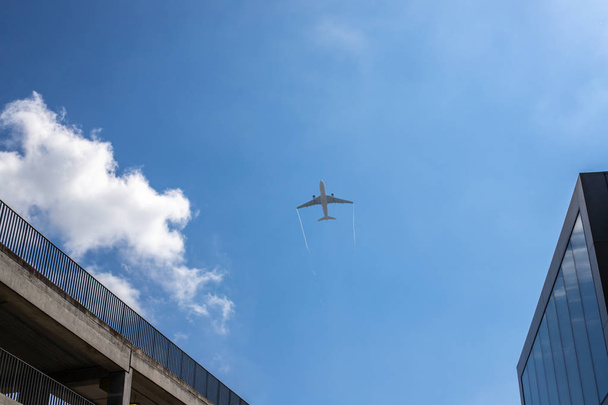 Airplan deja un rastro en el cielo azul. El avión está despegando sobre el puente y el edificio. Nube blanca en el cielo azul en el que vuela el avión
. - Foto, Imagen