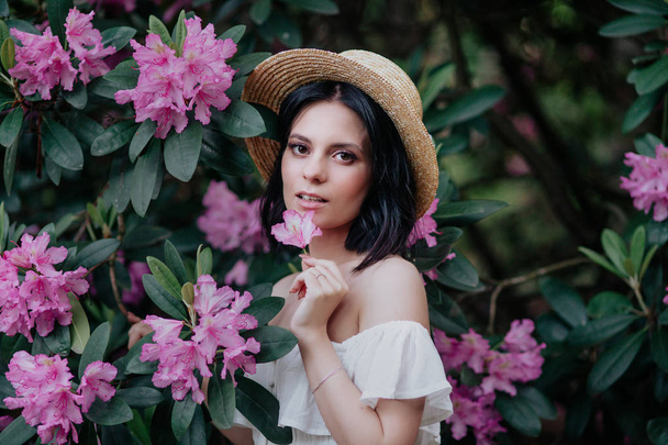 Outdoor portrait of young beautiful happy smiling woman in straw hat posing near flowering tree. - Valokuva, kuva