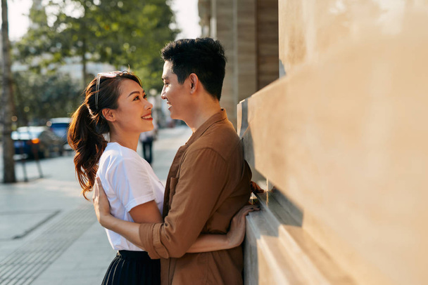 Visão traseira de um jovem casal abraçando em uma cidade de destino enquanto estava no distrito comercial perto de uma loja de sapatos de qualidade de luxo, ao ar livre
 - Foto, Imagem