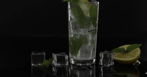 Acqua trasparente in vetro con foglie di menta verde e cubetti di ghiaccio su fondo nero
 - Filmati, video