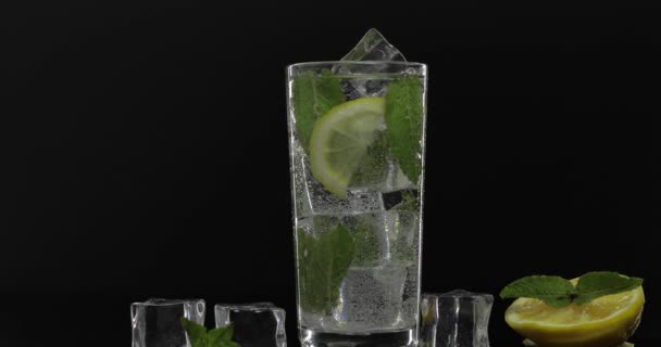 Чистая вода в стакане с зелеными листьями мяты и кубиками льда на черном фоне
 - Кадры, видео