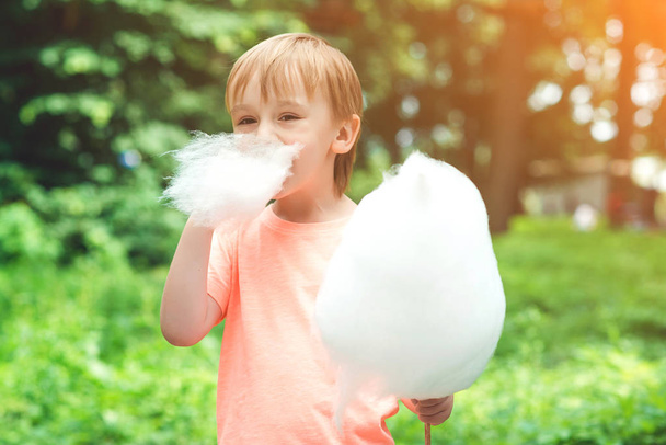 Happy child eating cotton candy. Cute little boy outdoors. Happy childhood - Фото, изображение