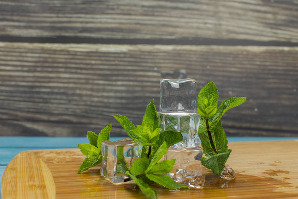 Ice cubes and mint leaves isolated on wooden cutting board - Фото, изображение