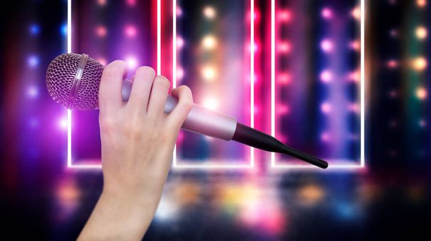 Naiskäsi pitelee yhtä mikrofonia karaokeklubin värikkäitä valoja vasten. Kirkas värikäs tausta hämärtyneillä neonvaloilla
 - Valokuva, kuva