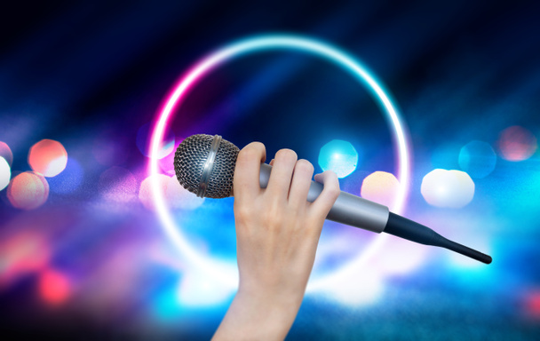 Una mano femenina sostiene un micrófono contra las luces coloridas de la escena del club de karaoke. Fondo colorido brillante con luces de neón borrosas
 - Foto, imagen