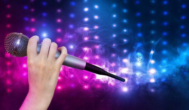 Bir kadın el Karaoke kulüp sahnesinin renkli ışıklar karşı bir mikrofon tutuyor. Bulanık Neon Işıklar ile parlak renkli arka plan - Fotoğraf, Görsel