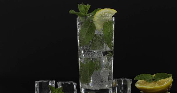 klares Wasser im Glas mit grünen Minzblättern und Eiswürfeln auf schwarzem Hintergrund - Foto, Bild