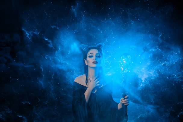 mysterious dark elf got terrible curse, charming girl with horns on head and glowing sparkling magic stick in hands, damned lady in green electric fire puts her hand on neck, creative art photo - Photo, image