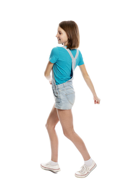Teen girl in denim overalls in a flying pose, full height. Isolated on a white background. - Foto, imagen