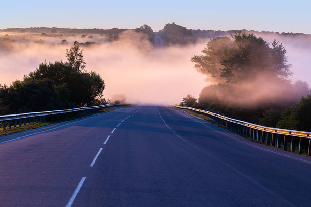 ранним утром туман в волне на летнем шоссе возле реки с рельсами охраны
 - Фото, изображение