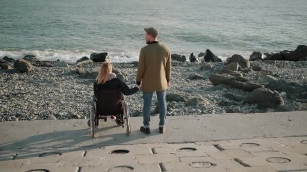 Femme en fauteuil roulant utilisateur et homme en bonne santé se tiennent la main et regardent le paysage marin
 - Séquence, vidéo