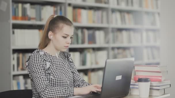 Vážná dívka student pracuje na notebooku s knihou v městské knihovně - Záběry, video