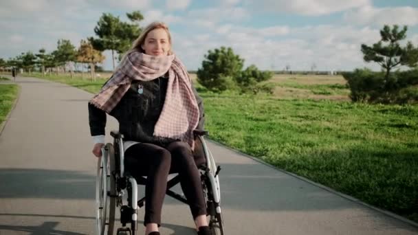Bacak ve omurga hastalığı olan bir kadın parkta tekerlekli sandalyeye biniyor, gülümsüyor. - Video, Çekim