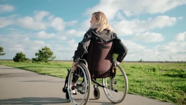 Adult disabled woman is driving her wheelchair in park area in sunny day - Footage, Video