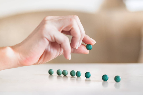 Vrouwelijke hand houden een Spirulina-pil naast pillen op een tafel. - Foto, afbeelding