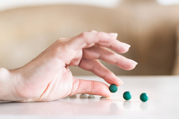 Kobieta ręka trzyma tabletkę Spirulina obok pigułki na stole. - Zdjęcie, obraz