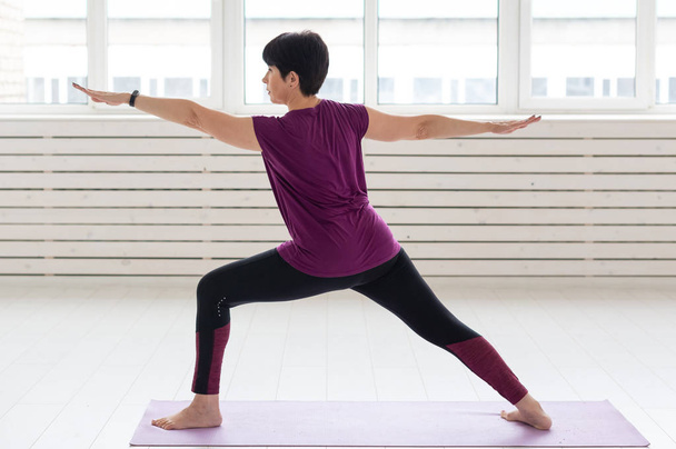 Persone, yoga, sport e assistenza sanitaria concetto donna di mezza età in piedi in guerriero su sfondo bianco
 - Foto, immagini