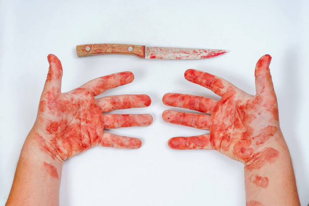 A man with a sharp knife in his hands on a white background. Bloodied hands on a light background. Dangerous melee weapons in the bloody hand of a person. Careless use of a kitchen knife. Blood knife - Photo, image