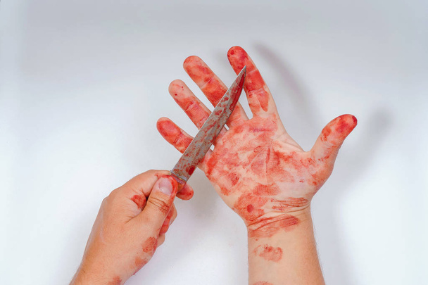 Un homme avec un couteau pointu dans les mains sur un fond blanc. Mains ensanglantées sur un fond clair. Dangereuses armes de mêlée dans la main d'une personne. Utilisation imprudente d'un couteau de cuisine. Couteau à sang
 - Photo, image