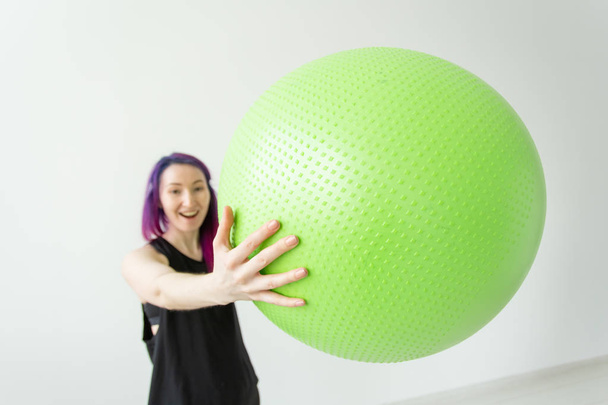 Θολή νέα θετική χαρούμενο κορίτσι χίππη κρατώντας μια πράσινη μπάλα στην αγκαλιά της κατά τη διάρκεια των μαθημάτων στο γυμναστήριο. Έννοια της γιόγκα, πιλάτες και Fitness. - Φωτογραφία, εικόνα