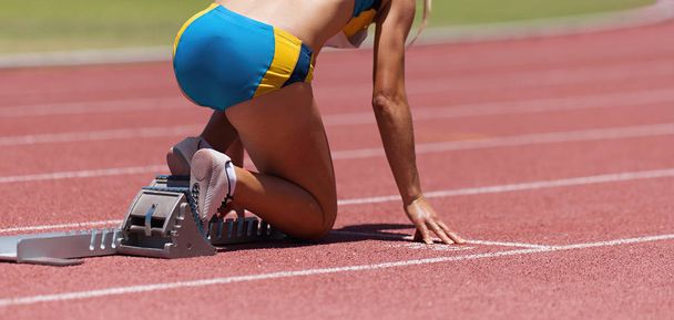 Женщина-спортсмен на стартовой позиции готова к старту и гонке, готова к бегу по гоночному треку
 - Фото, изображение