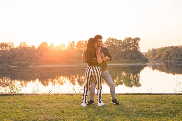 Romantic, social dance, people concept - young couple dancing bachata near the lake in sunny day - Photo, Image
