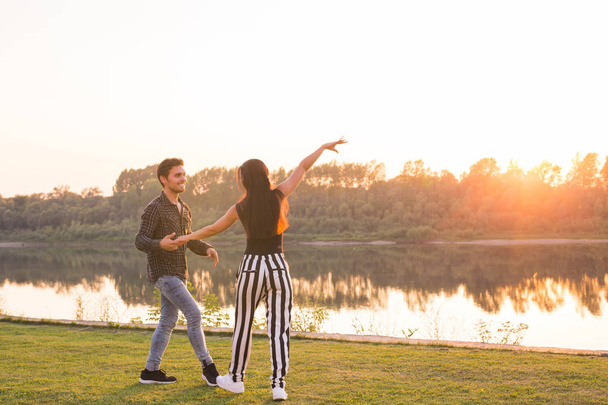 Romantic, social dance, people concept - young couple dancing bachata near the lake in sunny day - Photo, Image