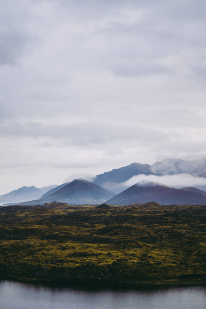 Kaunis vihreä islantilainen maisema usvaisine vuorineen horisontissa
 - Valokuva, kuva