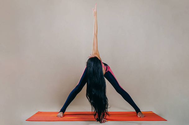 Beautiful slim fit woman coach stands in asanas on a bright rug  - 写真・画像