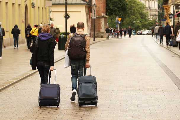 A young couple will ride down the street of the old town with tourist suitcases on wheels. Grodskaya street in the rain. Travel to historical places. Honeymoon after the wedding - Fotoğraf, Görsel