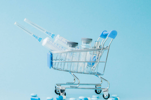 Pills and medical injection in shopping trolley on blue backgrou - Zdjęcie, obraz