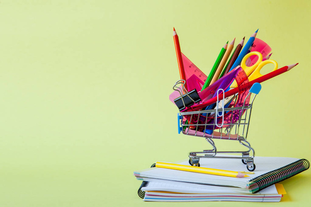 Shopping cart with different stationery on the yellow background - Φωτογραφία, εικόνα