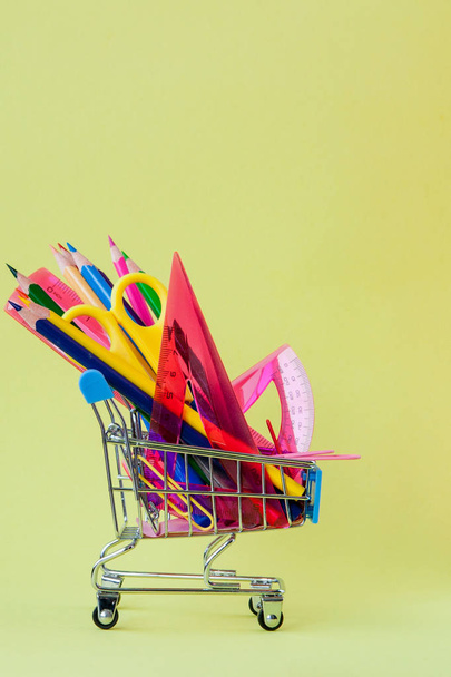 Shopping cart with different stationery on the yellow background - Photo, Image