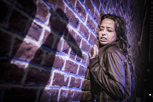 Мужская фигура тени с ножом угрожает напуганной молодой женщине против кирпичной стены
 - Фото, изображение