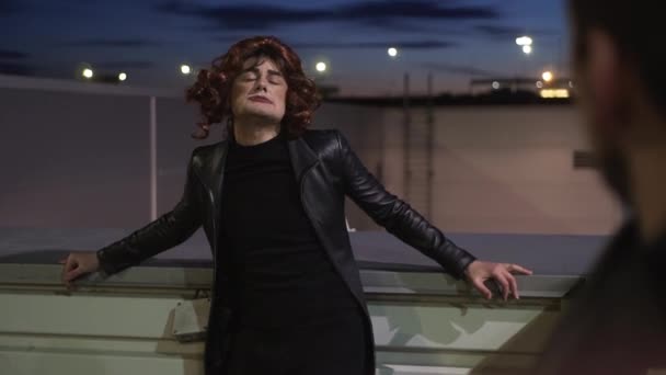 Charyzmatyczny facet ubrany jak kobieta, ubrany w czarne ubrania i peruki, śpiewa na zewnątrz - Materiał filmowy, wideo