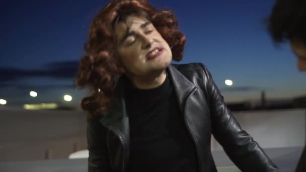 Hombre con peluca vestido como mujer con maquillaje emocionalmente canta junto a otro chico
 - Metraje, vídeo