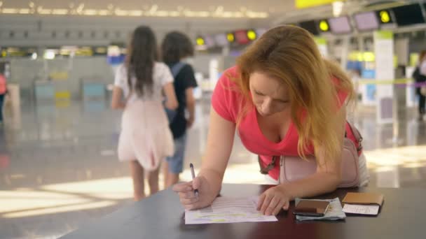 έννοια της μεταφοράς Ασυνόδευτου παιδιού. Μια γυναίκα με δύο εφηβικά παιδιά συμπληρώνει έγγραφα στο αεροδρόμιο - Πλάνα, βίντεο