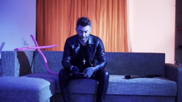 Attractive man with stylish hair cut in leather jacket sits on sofa and sings. - Filmmaterial, Video