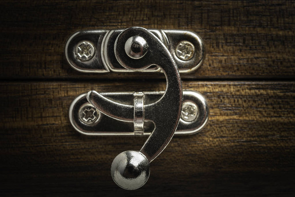 A close-up or macro look of a silver-color metal sliding lock latch installed on a polished wooden box in horizontal image format. - Photo, Image