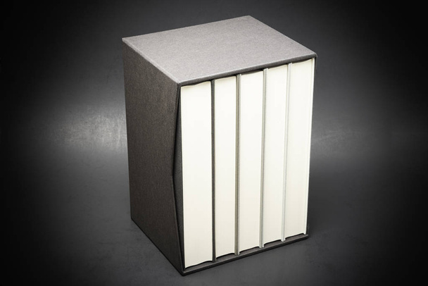 ein Satz von fünf monochromen, leinengebundenen Büchern, die in einem schwarzen harten Kartonschuber auf einem leicht abgestuften und subtil strukturierten dunklen Hintergrund aufbewahrt werden. - Foto, Bild