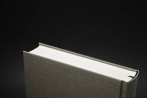 eine Nahaufnahme des oberen Teils eines in Leinen gebundenen Buches mit permanentem schwarzen Lesezeichen aus Seide auf dunklem Hintergrund. - Foto, Bild