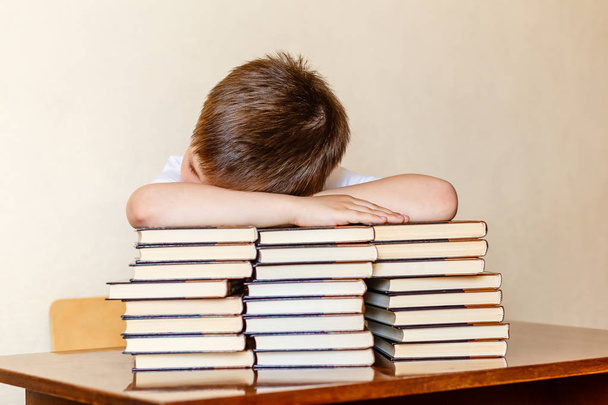 the child sits at the table, putting his head on the books. - Foto, afbeelding