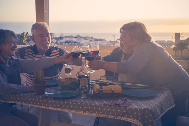 Aktivní starší lidé koncept se skupinou dospělých přátel, kteří spolu večeří doma na terase s výhledem na město a oceán - Fotografie, Obrázek