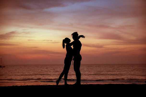 jong stel zoenen op een tropisch strand, zonsondergang op de achtergrond - Foto, afbeelding