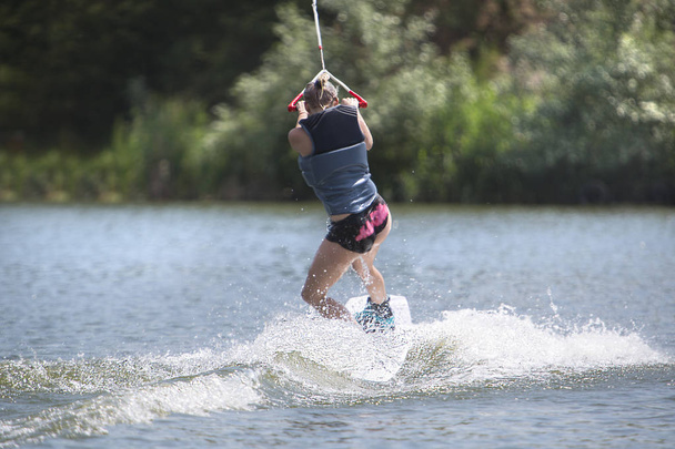 Young pretty slim woman riding a wakeboard on the lake in summer - Photo, Image