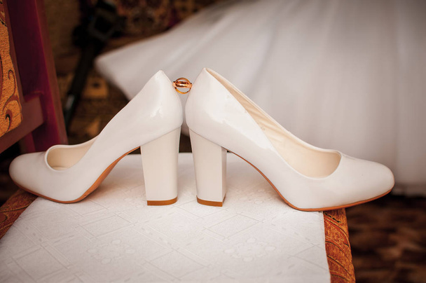 Par de anéis de casamento dourados entre um par de sapatos brancos
 - Foto, Imagem