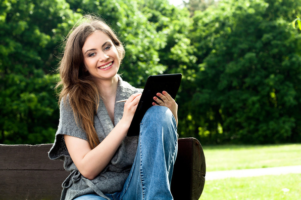 Beautiful woman working with a tablet in park - 写真・画像