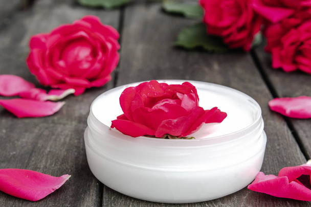 Naturalne kosmetyki kwiatowe z czerwonymi różowymi kwiatami do pielęgnacji twarzy i ciała w szklanym słoiku na drewnianym tle rustykalnym - Zdjęcie, obraz